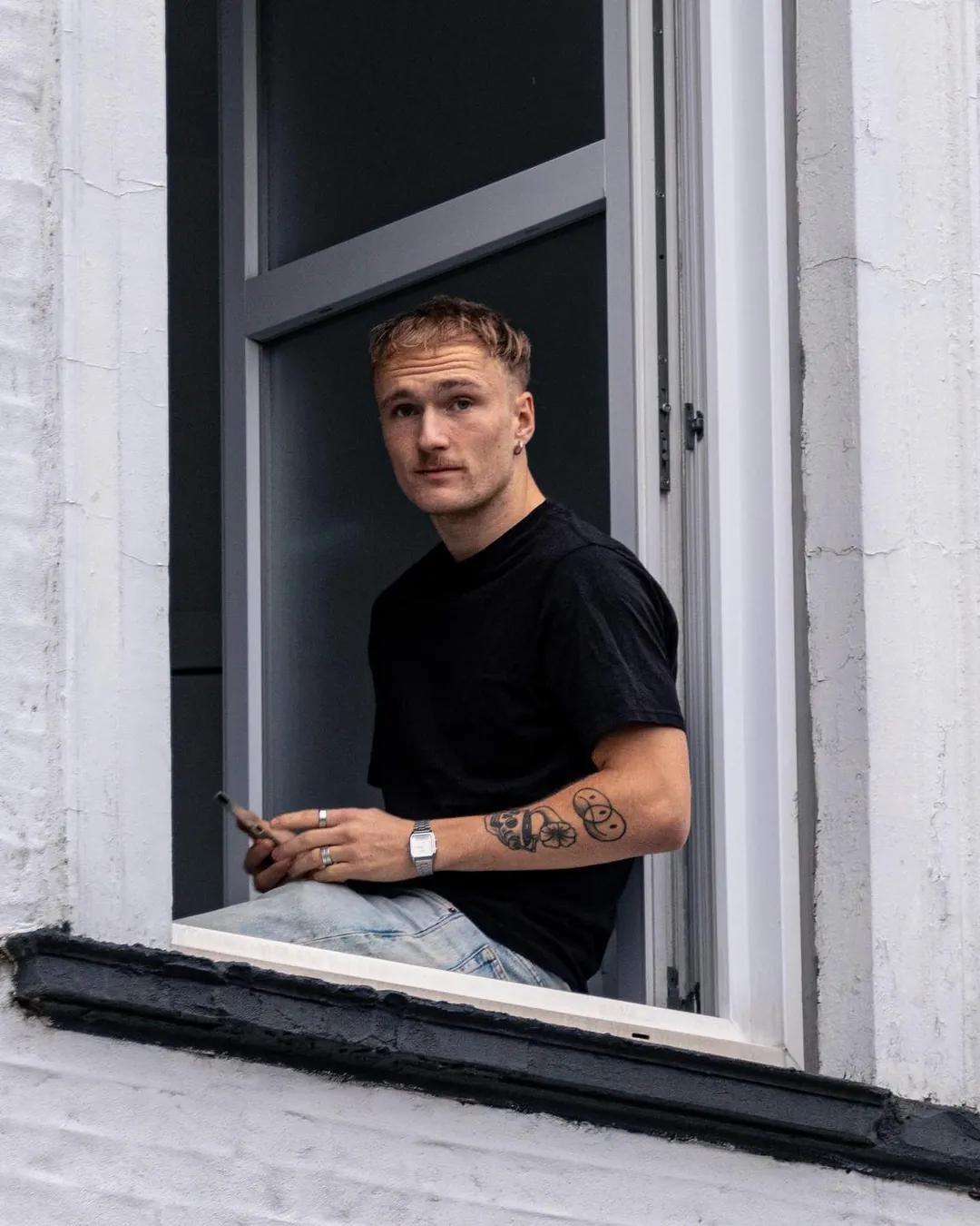 Ung mand fotograferet i &aring;bent vindue i hvid murstensfacade